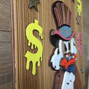 May include: A wooden wall art piece featuring a cartoon character wearing a red, white, and blue hat with stars. The character is holding a magnifying glass and has a dollar sign dripping down the side of the piece.