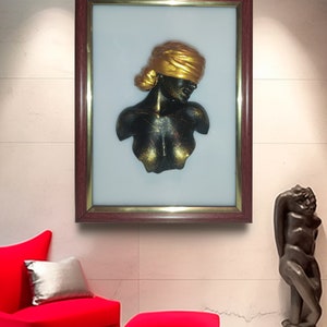 May include: A framed artwork featuring a black and gold sculpture of a woman's bust. The sculpture is set against a white background and is framed in a dark wood frame.