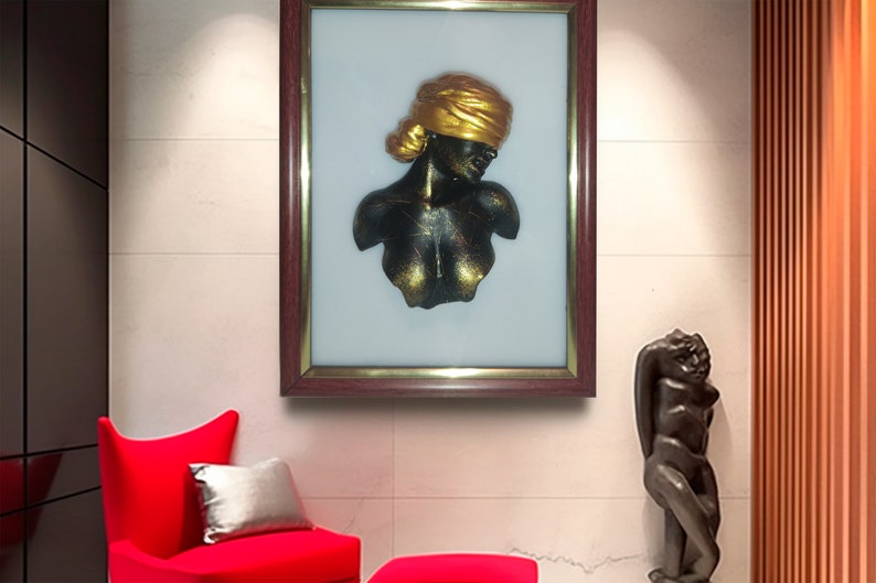 May include: A framed artwork featuring a black and gold sculpture of a woman's bust. The sculpture is set against a white background and is framed in a dark wood frame.