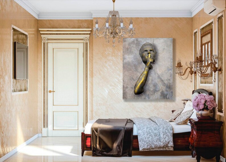 May include: A gold-toned sculpture of a person with their finger to their lips, suggesting silence. The sculpture is mounted on a textured, grey canvas.