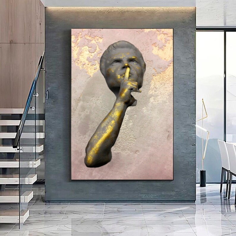 May include: A gold and grey sculpture of a person with their finger to their lips, on a pink and gold background.