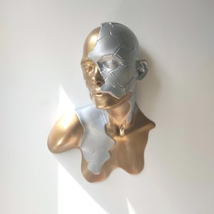 May include: A gold and silver bust sculpture of a person with a cracked face. The sculpture is a modern art piece with a unique and abstract design.