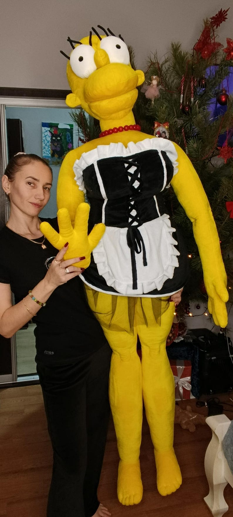 May include: A large, yellow plush figure resembling a cartoon character, wearing a black and white maid outfit with a red beaded necklace. The figure has large yellow hands and feet.