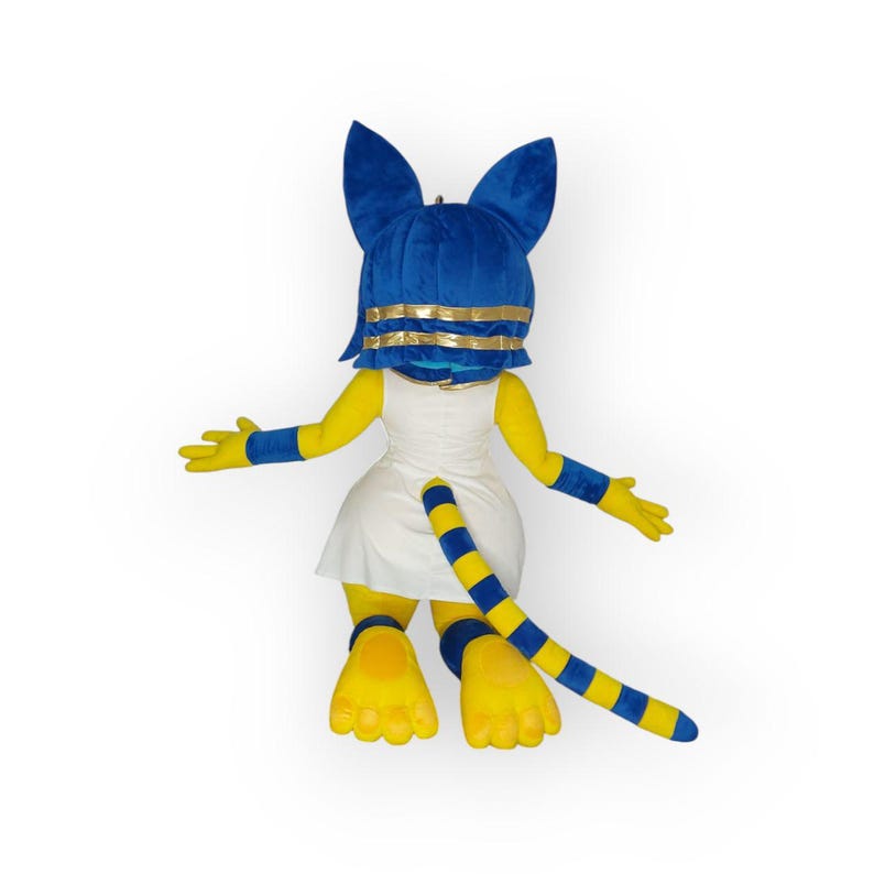May include: A plush mascot costume of a yellow cat with blue ears and a blue and gold headpiece. The costume is wearing a white dress and has a blue and yellow striped tail.