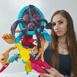 May include: A colorful plush creature with multiple arms and a central head. The plush features a variety of colors, including blue, red, yellow, and pink. The creature has a unique, abstract design.