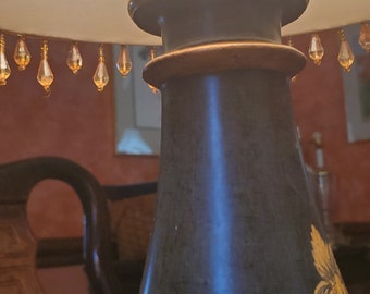 May include: Close-up of a vintage lamp with a black base adorned with gold floral designs. The lamp features a brass fixture and a lampshade with hanging crystal accents. The lamp is a decorative lighting fixture.