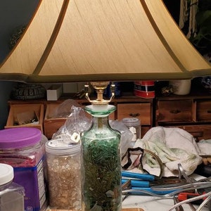 May include: A green glass lamp base filled with green and white glass beads. The lamp has a beige fabric lampshade.