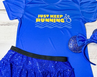 Może przedstawiać: Niebieska koszulka sportowa z napisem "JUST KEEP RUNNING" w kolorze żółtym i białym. Na zdjęciu znajduje się również niebieska spódnica z cekinami i niebieska opaska do włosów z cekinową kokardą. Strój jest przeznaczony do biegania lub na imprezy tematyczne.