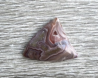 May include: A triangular shaped agate cabochon with brown, white, and pink banding. The agate has a natural, polished finish.