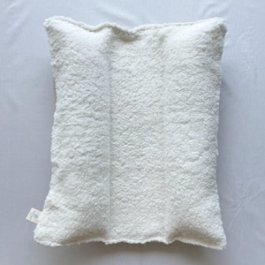 May include: A white, rectangular pillow with a textured, plush surface. The pillow has a soft, fluffy appearance and is made of a thick, cozy material. The pillow is designed for comfort and relaxation.