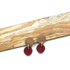 May include: A pair of earrings with a wooden circle and a burgundy felt circle dangling from a gold hoop.
