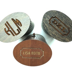 K&ouml;nnte beinhalten: Drei Holzkisten mit gravierten Namen. Die Kisten sind oval geformt und haben ein Latten-Design. Die Namen sind "Lisa Roth", "D.K.L." und "K.L.M."