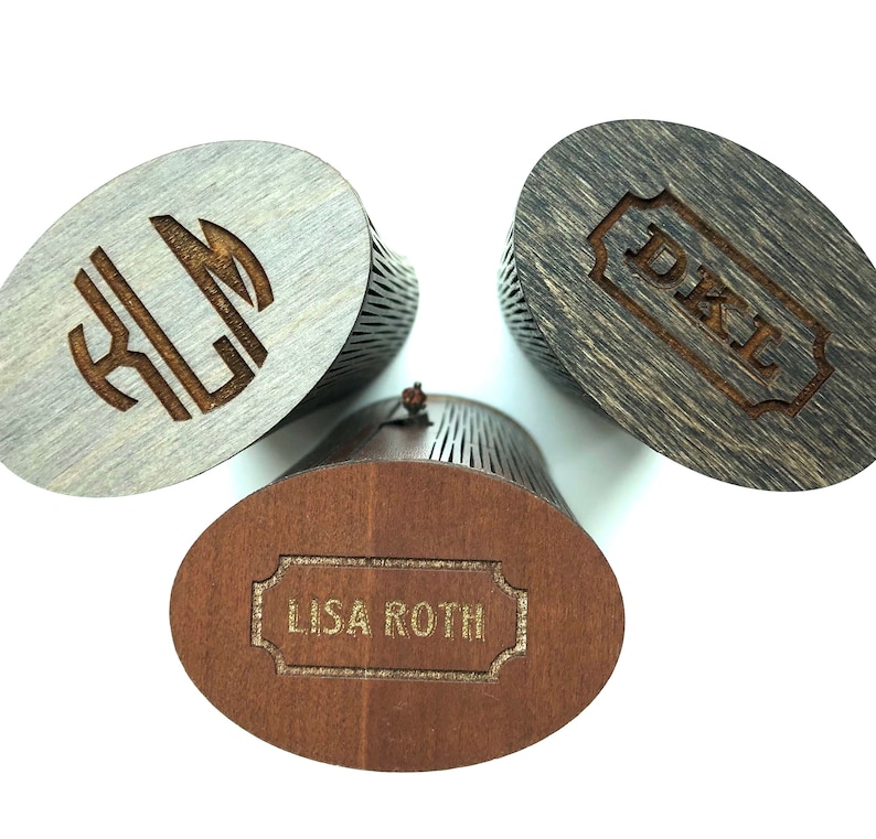 K&ouml;nnte beinhalten: Drei Holzkisten mit gravierten Namen. Die Kisten sind oval geformt und haben ein Latten-Design. Die Namen sind "Lisa Roth", "D.K.L." und "K.L.M."