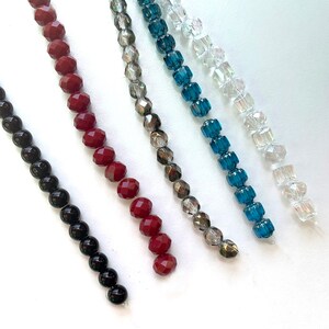 K&ouml;nnte beinhalten: F&uuml;nf Perlenstr&auml;nge, jeder mit einer anderen Farbe und einem anderen Stil. Die Str&auml;nge beinhalten schwarze, rote, graue, blaue und klare Perlen.