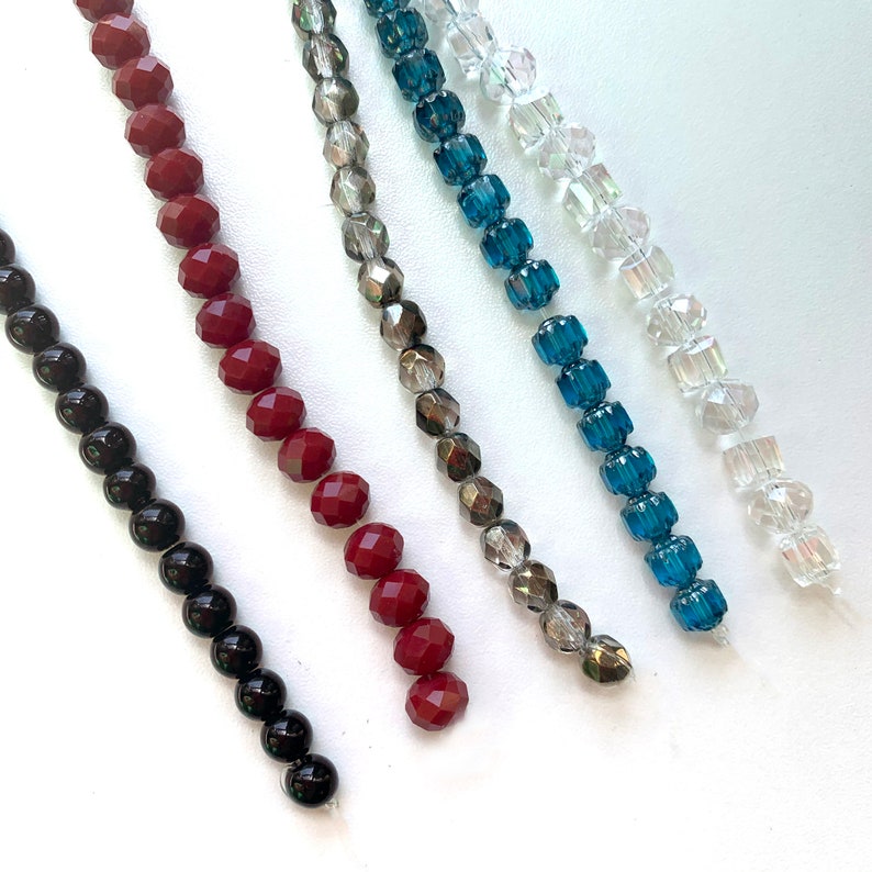 K&ouml;nnte beinhalten: F&uuml;nf Perlenstr&auml;nge, jeder mit einer anderen Farbe und einem anderen Stil. Die Str&auml;nge beinhalten schwarze, rote, graue, blaue und klare Perlen.