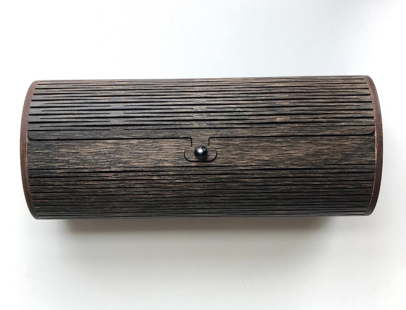 K&ouml;nnte beinhalten: Eine zylindrische Holzkiste mit dunkelbrauner Oberfl&auml;che und einem schwarzen Verschluss. Die Kiste hat ein gerilltes Muster auf der Au&szlig;enseite.