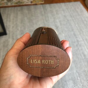 K&ouml;nnte beinhalten: Eine Holzkiste mit einer goldenen Inschrift, die "LISA ROTH" lautet. Die Kiste hat ein gerilltes Design und ist aus dunkelbraunem Holz.