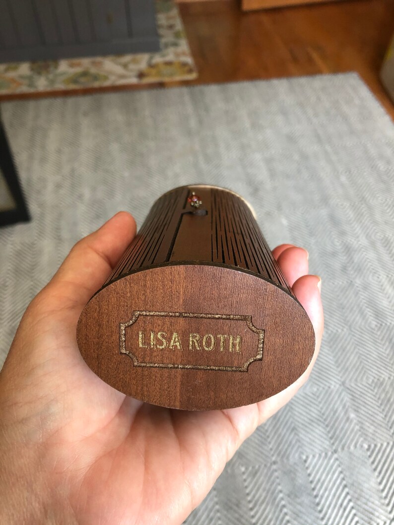 K&ouml;nnte beinhalten: Eine Holzkiste mit einer goldenen Inschrift, die "LISA ROTH" lautet. Die Kiste hat ein gerilltes Design und ist aus dunkelbraunem Holz.
