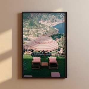 Può includere: Un ombrellone a strisce rosa e bianche offre ombra a due sdraio rosa su un prato verde con vista su un panorama costiero pittoresco.