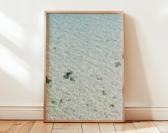 May include: A framed photograph of a turquoise blue ocean with ripples and light reflecting on the surface. The water is shallow and clear, revealing the sandy bottom.