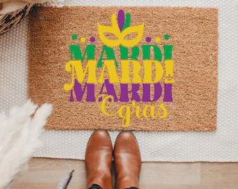 May include: A brown doormat with the text "Mardi Gras" in yellow, green, and purple lettering. The text is stacked on top of each other, with the word "Mardi" repeated three times. A purple and yellow mask is above the text.
