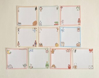 May include: Set of ten Christmas-themed grid paper notepads with various illustrations, including a snowman, a nutcracker, a gingerbread man, and a Christmas tree. Each notepad has a white background with a light pink, blue, or green border.