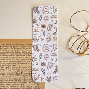 May include: A white bookmark with a repeating pattern of teapots, teacups, socks, pies, mushrooms, candles, and flowers. The text "forest", "cotton", and "catto" appears on the bookmark.