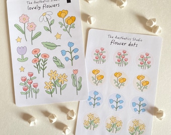 May include: Two sheets of stickers featuring flower designs. The first sheet has the text "The Aesthetics Studio lovely flowers" and features various flowers in pink, yellow, and blue. The second sheet has the text "The Aesthetics Studio flower dots" and features small circular stickers with yellow, blue, and pink flowers.