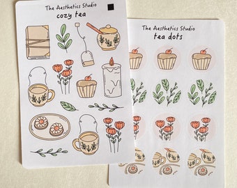 May include: Two sheets of stickers with a tea theme. The first sheet has the text "The Aesthetics Studio cozy tea" and features illustrations of teacups, tea bags, a candle, flowers, and pastries. The second sheet has the text "The Aesthetics Studio tea dots" and features illustrations of teacups, flowers, and leaves in circular frames.