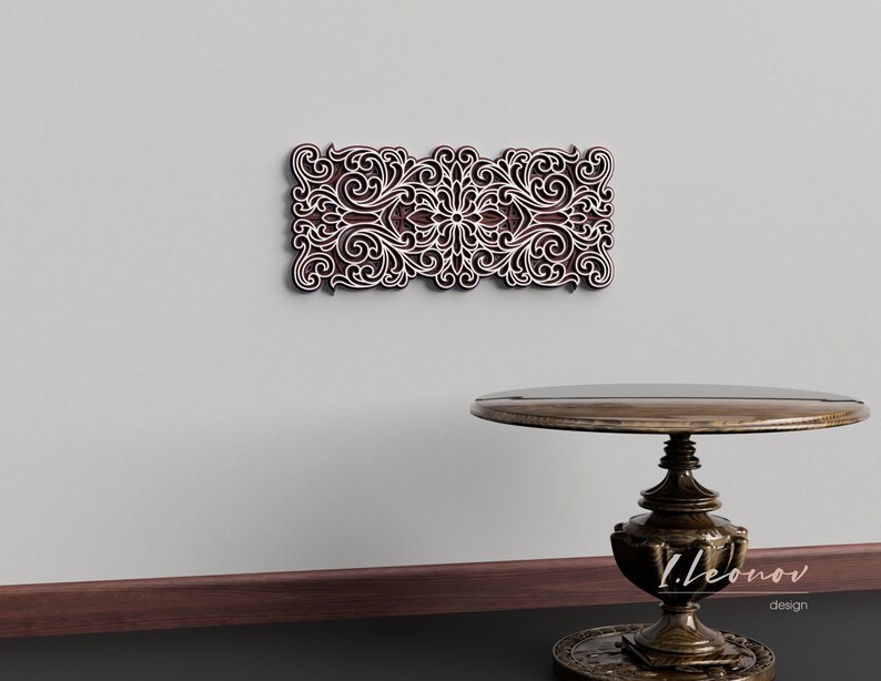 May include: A white wall with a brown wooden decorative wall panel featuring a carved floral design. A dark brown wooden table with a round top and a pedestal base sits in front of the wall.