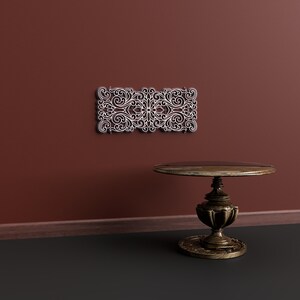 May include: A dark brown wooden table with a round top and ornate legs sits on a dark grey floor in front of a maroon wall. A white decorative wall panel with a floral design is mounted on the wall.