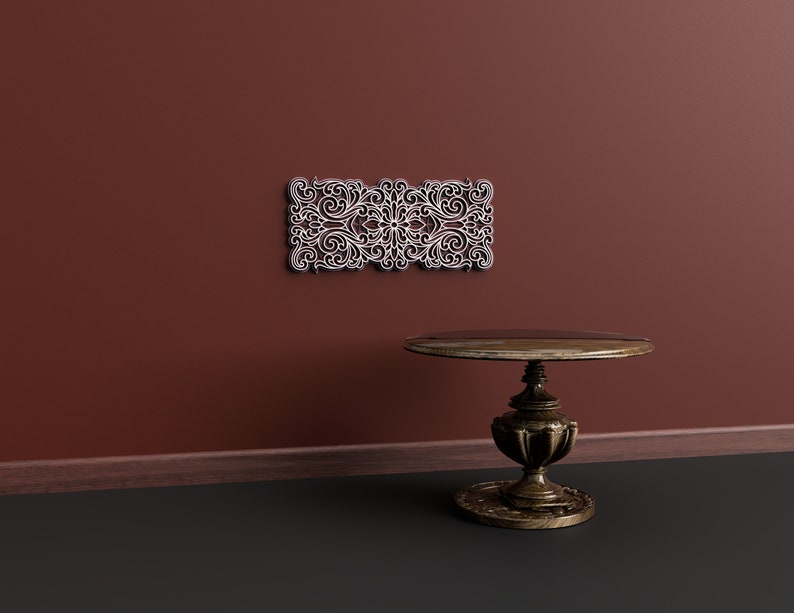 May include: A dark brown wooden table with a round top and ornate legs sits on a dark grey floor in front of a maroon wall. A white decorative wall panel with a floral design is mounted on the wall.