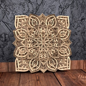 May include: A detailed wooden mandala with intricate cutouts, creating a layered and dimensional design. The mandala is a light brown color and has a symmetrical pattern.