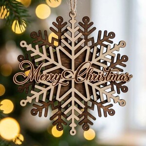 May include: Wooden snowflake Christmas ornament with the words "Merry Christmas" in a cursive font. The ornament is made of light and dark brown wood and hangs from a natural twine string. The snowflake design is intricate and detailed.