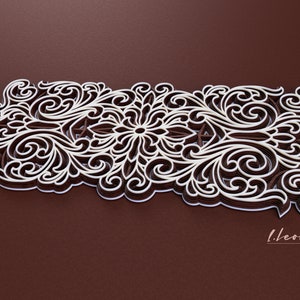 May include: An intricate paper cut design in white and brown, featuring a floral pattern. The design is layered and has a 3D effect. The background is a dark brown.