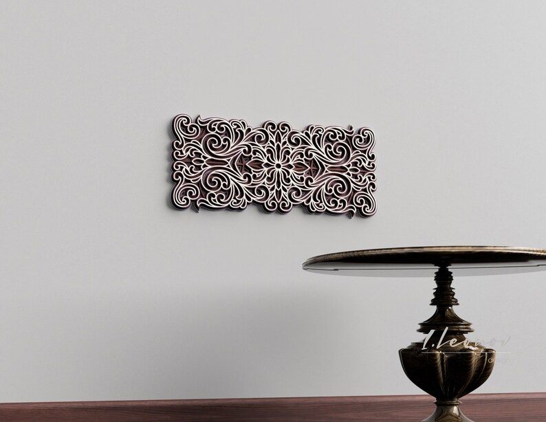 May include: A decorative wall hanging with a white intricate design on a brown background. The design features a floral pattern with swirls and curves.