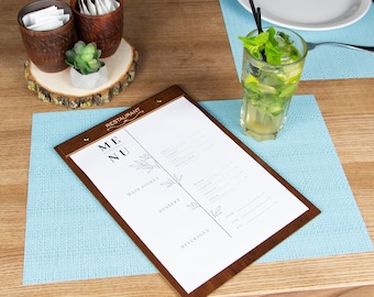 May include: A wooden clipboard menu with the words "Restaurant Menu" printed on the front. The menu is on a blue placemat with a glass of mojito on the table.