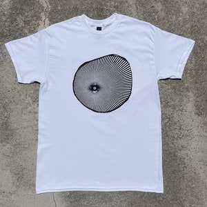 Puede incluir: Camiseta blanca con un gráfico en blanco y negro de un diseño circular con un ojo central.