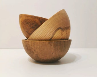 May include: Three wooden bowls of varying sizes, stacked on top of each other. The bowls are made of light brown wood with a natural grain pattern.