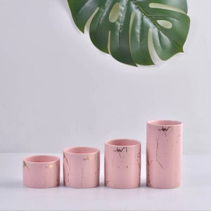 May include: Four pink ceramic cylinder vases with gold marbling. The vases are arranged in order of size, with the largest vase on the right and the smallest vase on the left.