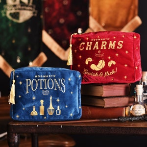 May include: Two velvet Hogwarts-themed makeup bags. The blue bag says "Hogwarts™ Potions Designed by Severus Snape" with gold stars and a gold tassel. The red bag says "Hogwarts™ Charms Professor Flitwick Swish & flick!" with gold stars and a gold tassel.