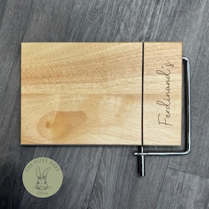 May include: A wooden cheese board with a built-in wire cheese cutter. The board is engraved with the name "Ferdinand's". The board is made by The Olive Hare Gift Co.