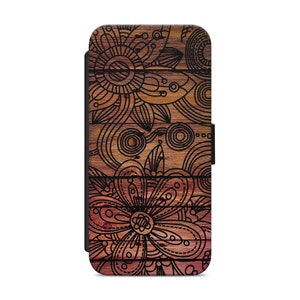 Pode incluir: Uma capa de telefone com fundo de madeira e desenhos florais pretos. A capa tem uma aba que cobre a tela do telefone.