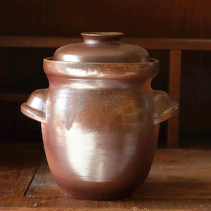 Puede incluir: Un tarro de cerámica marrón con tapa, con dos asas laterales. El tarro tiene un acabado brillante y una forma redondeada, adecuado para el almacenamiento de alimentos o uso decorativo. La tapa encaja perfectamente.