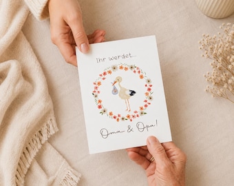 May include: A white rectangular greeting card featuring a central illustration of a stork carrying a blue bundle, surrounded by a circular wreath of small orange and pink flowers. The text reads "Ihr werdet..." at the top and "Oma & Opa!" below.