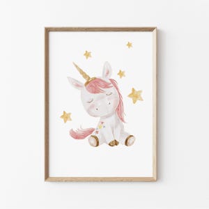 Könnte beinhalten: Aquarellillustration eines sitzenden Einhorns mit goldenem Horn und rosa Mähne und Schweif. Das Einhorn ist von goldenen Sternen umgeben. Das Kunstwerk ist in einem hellbraunen Holzrahmen gerahmt, ideal für ein Kinderzimmer.