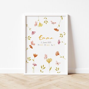 K&ouml;nnte beinhalten: Ein gerahmter Aquarelldruck mit dem Namen "Emma" in goldener Schrift, umgeben von zarten Blumen und Schmetterlingen in Rosa-, Gelb- und Oranget&ouml;nen. Datum und Uhrzeit sind ebenfalls enthalten.