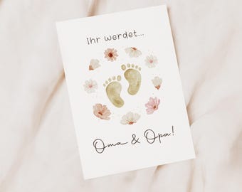 May include: A white card with the text "Ihr werdet..." and "Oma & Opa!" in black script. The card features two tan baby footprints surrounded by watercolor flowers in pink and white.