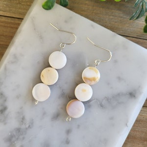 May include: A pair of silver earrings with three white and brown shell beads on each earring.
