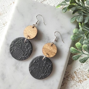 May include: A pair of dangle earrings with a black floral design and a wood accent. The earrings are made of polymer clay and wood.